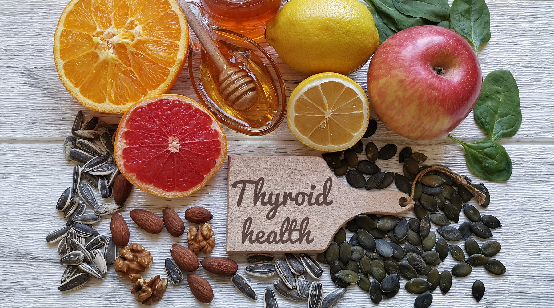 A wooden table with an arrangement of fruit, nuts and honey surrounding a 'thyroid health' note