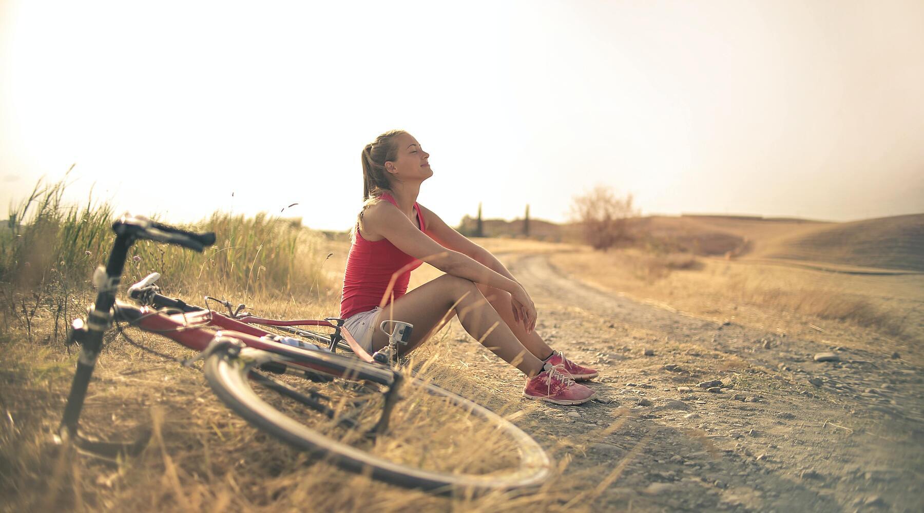 Woman sitting on ground relaxing next to her bike during an outdoor workout.