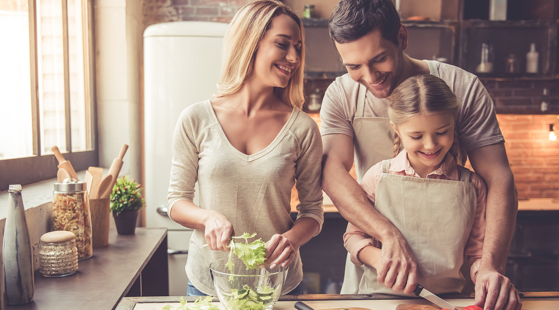 Healthy parents with a daughter in a kitchen making a salad and eating vegetables.
