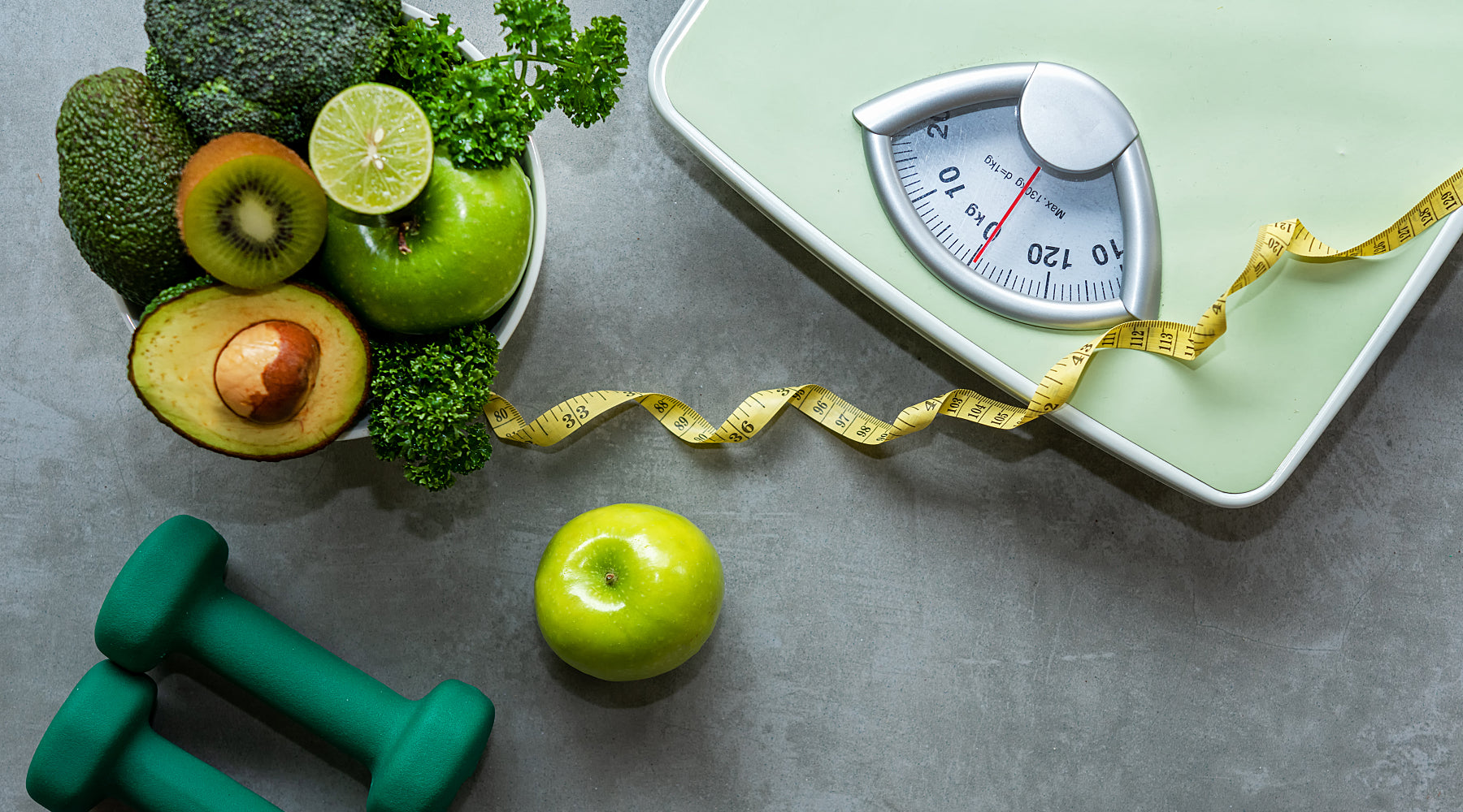 A scale, hand weights and a bowl of healthy foods