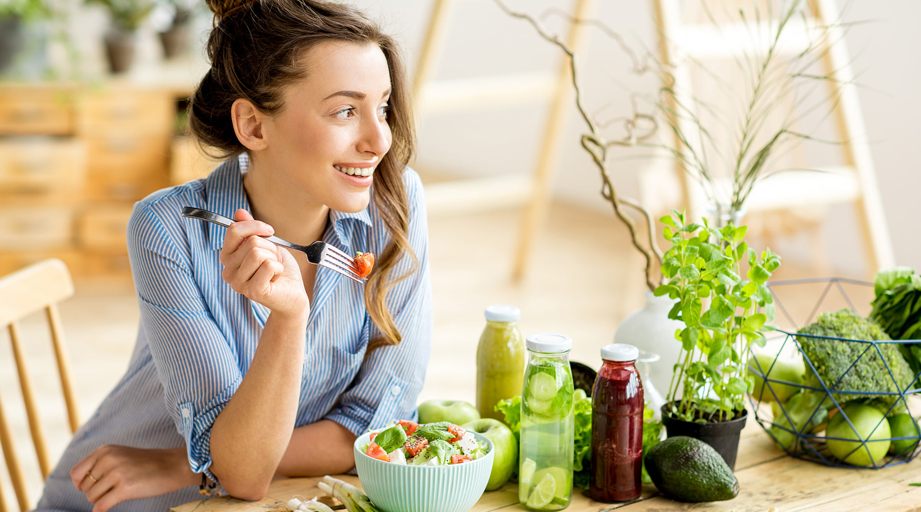 Woman seated at a table covered in green vegetables, eating a bowl of salad