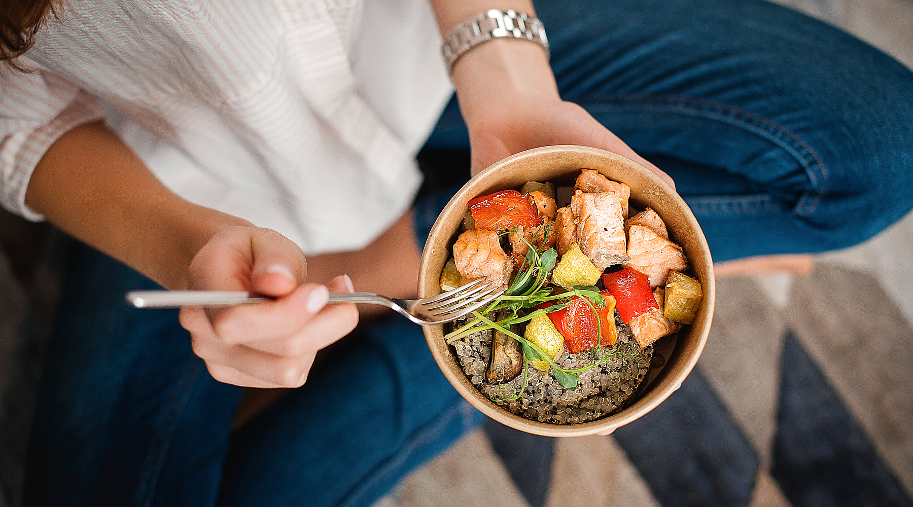 Woman sitting on the floor holding a healthy whole food meal in a bowl.