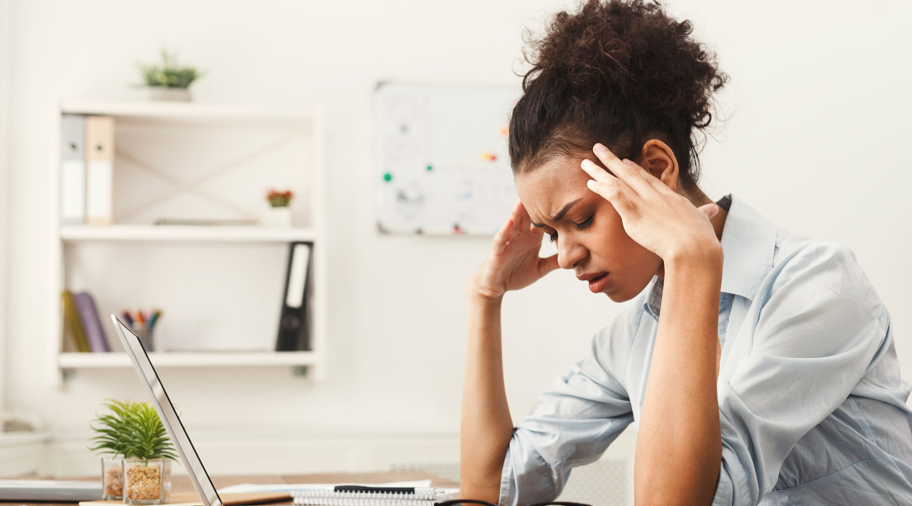 Woman with migraine sits at desk with head in hands