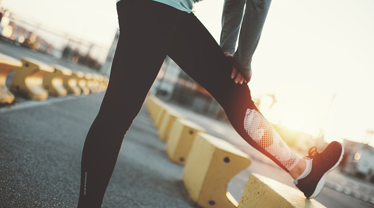 Woman in athletic wear stretches her hamstring before a run on a cobbled street in the morning.