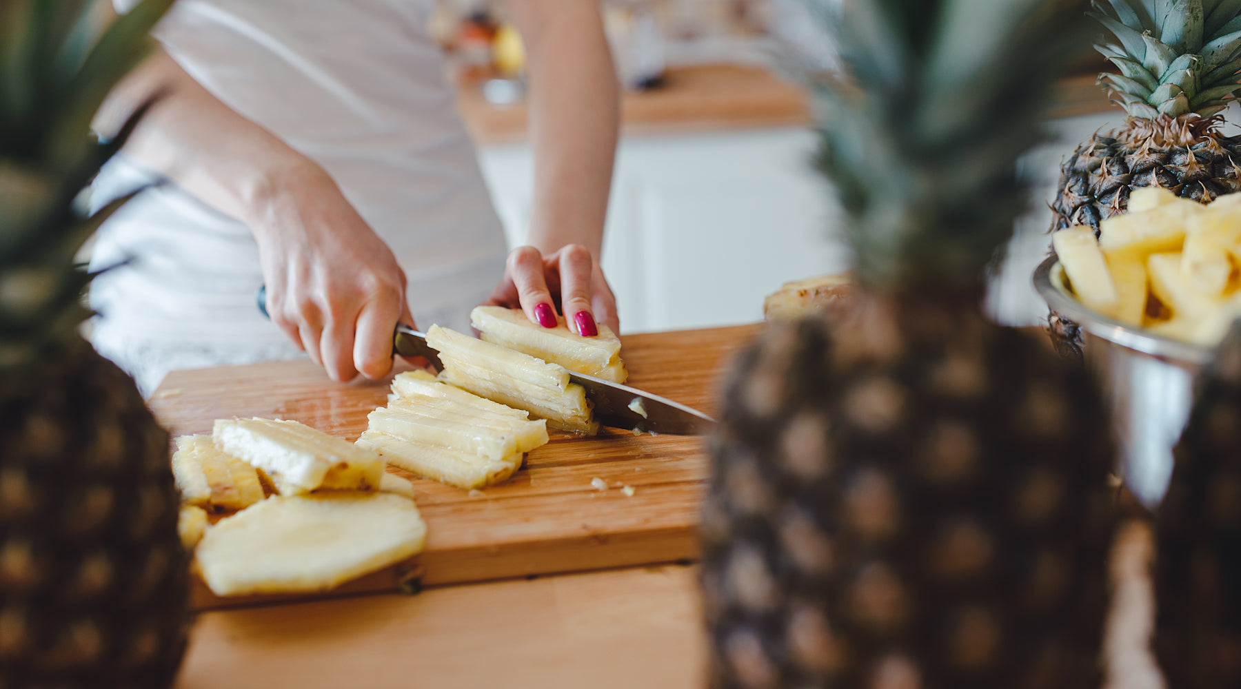 A person cutting up a pineapple with a knife.