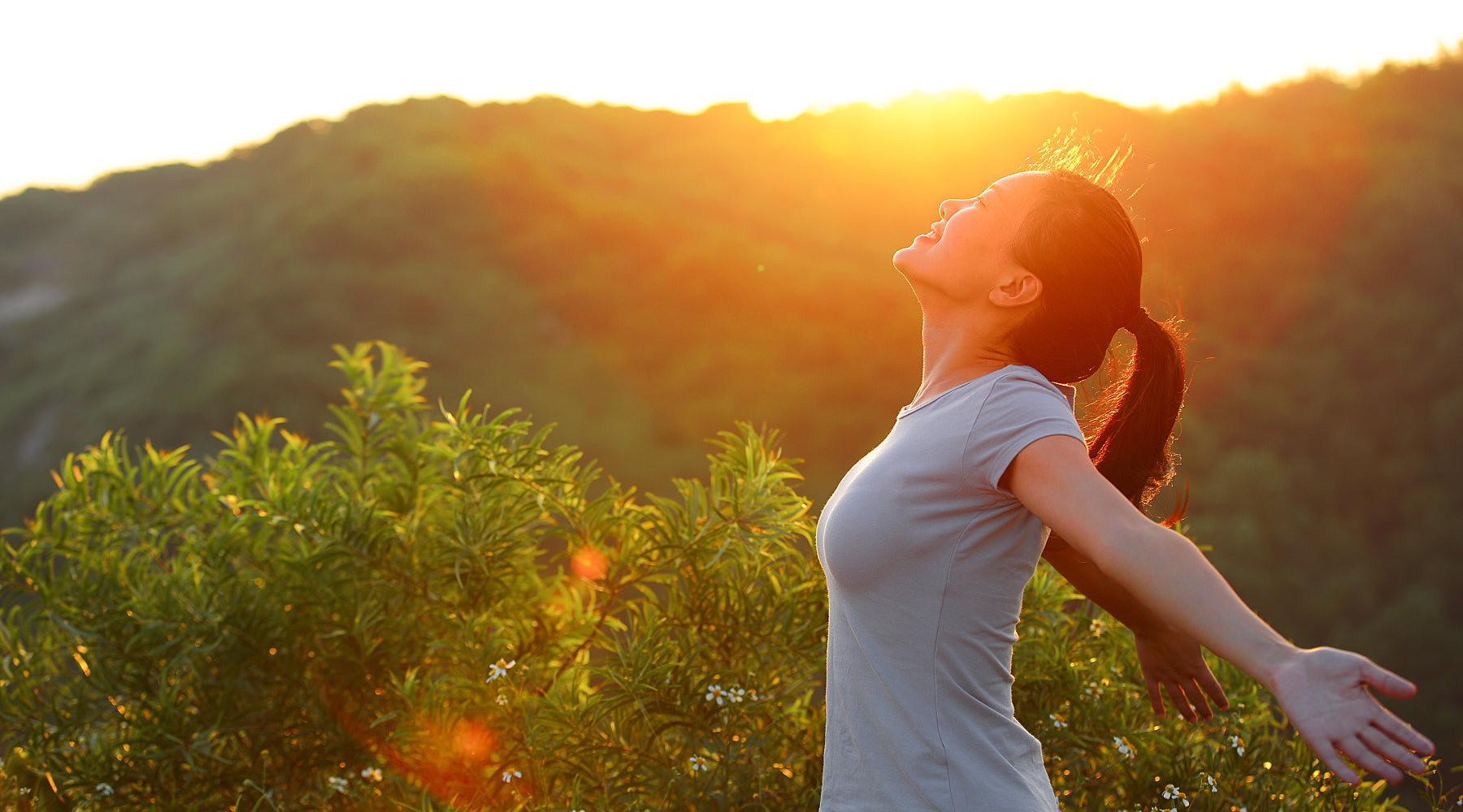 Woman standing in with her arms open and her eyes closed enjoying the sunshine.