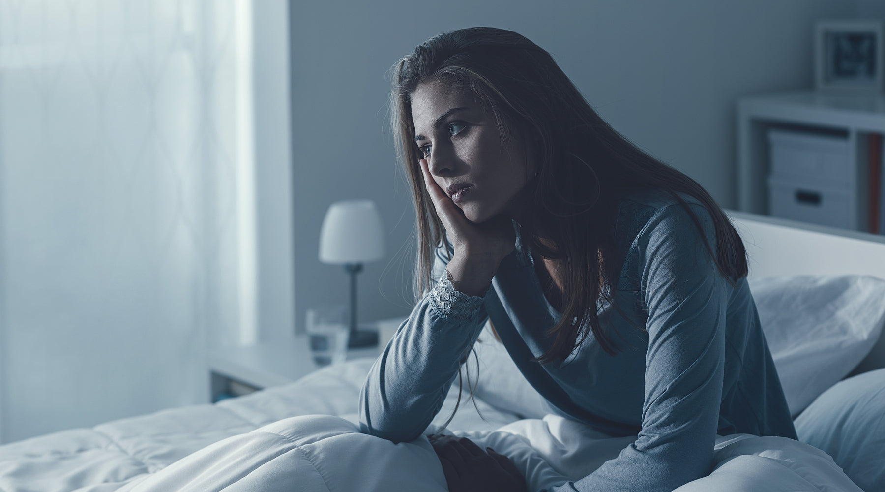 Tired woman struggling with chronic fatigue sits up in bed